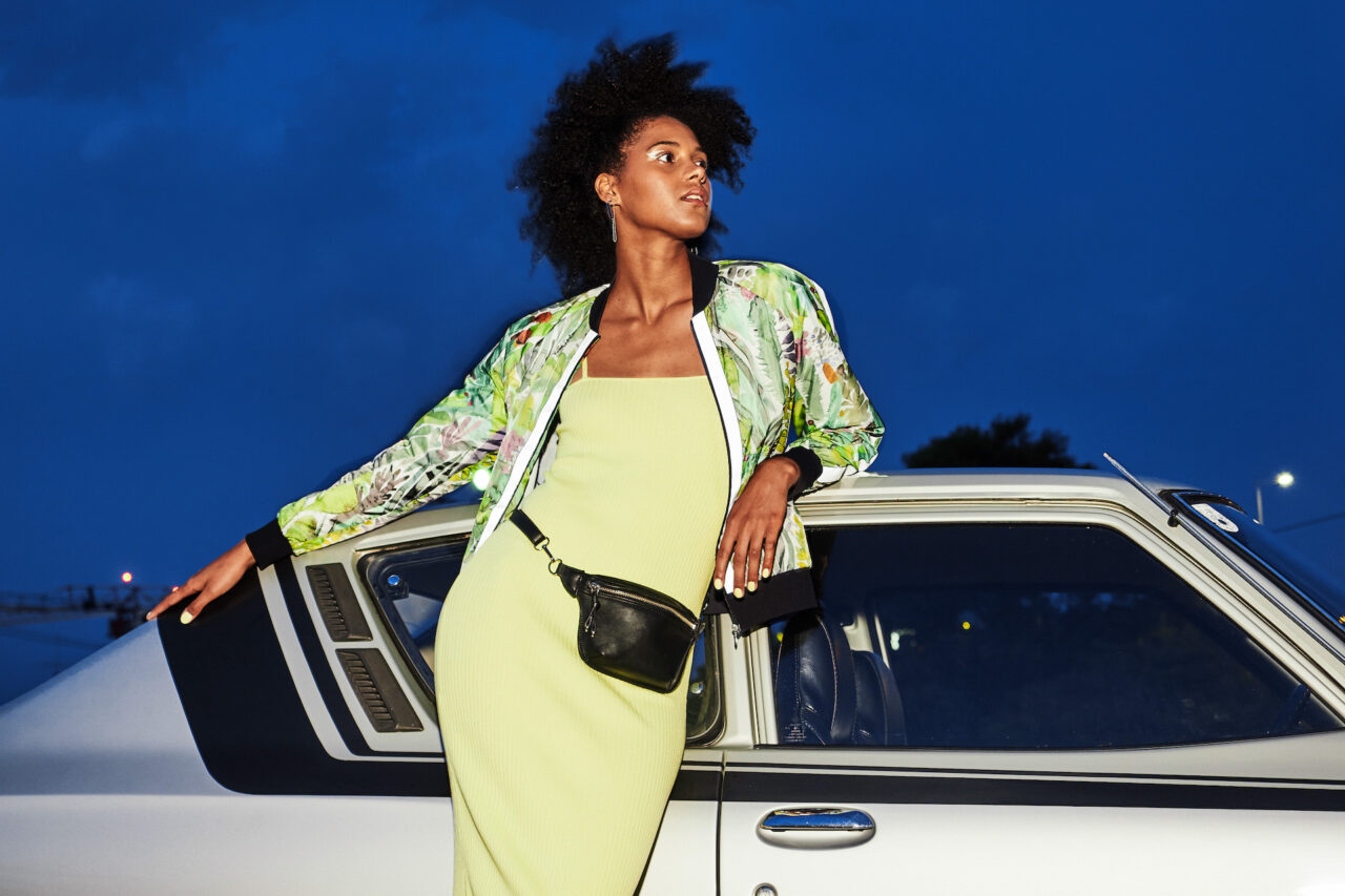 Frau in der Dämmerung mit einer leichten bunten Sommerjacke an einem Oldtimer angelehnt